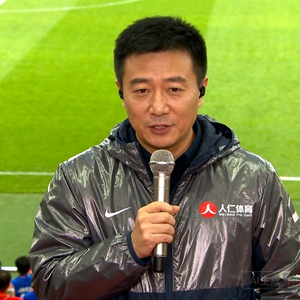 内容主编王晓东在赛事现场手持麦克风进行报道，身穿印有人人体育Logo的冲锋衣，背景为球场草坪